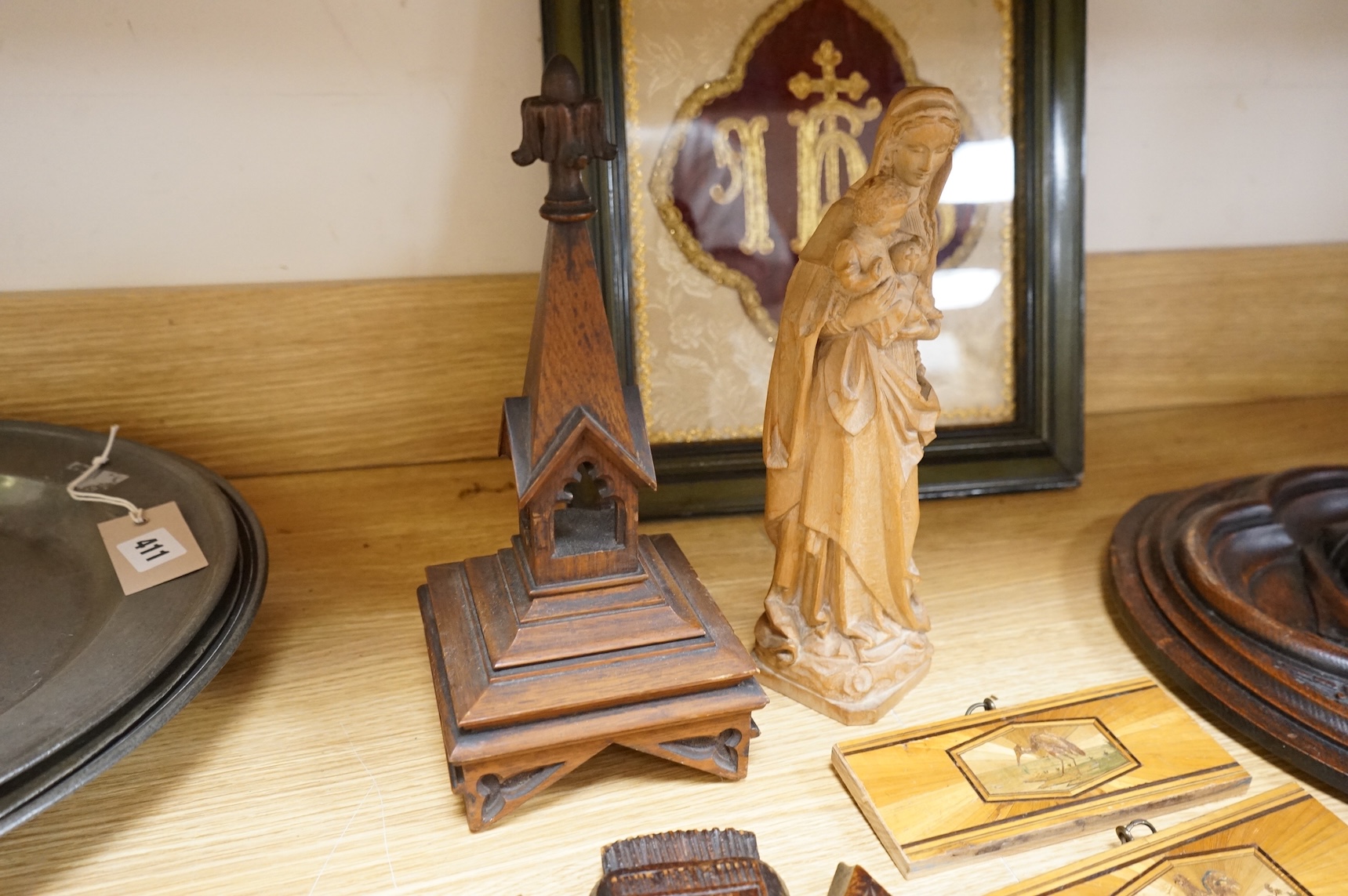 A pair of Gothic revival oak wall plaques, a Black Forest carved barometer, a Virgin and child figure, an IHS embroidered panel, two straw worked panels and a carved finial, barometer 47cm high